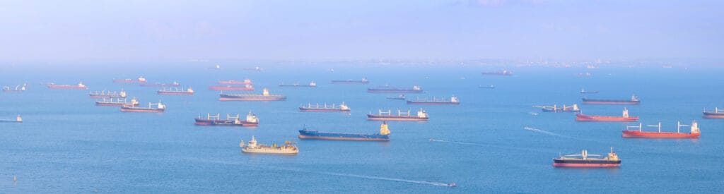 Panoramic view of Singapore harbor with many cargo ships at sunset.